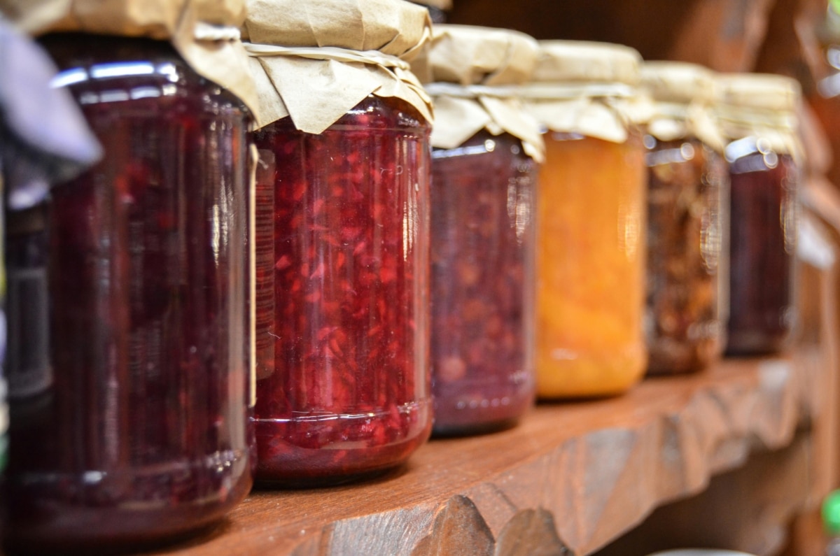 A close-up view of various homemade jam jars lined up on a wooden shelf.