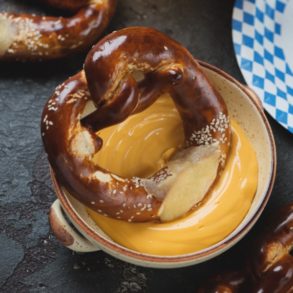 Pretzels with cheese dipping sauce and beer, vertical shot on a brown stone background